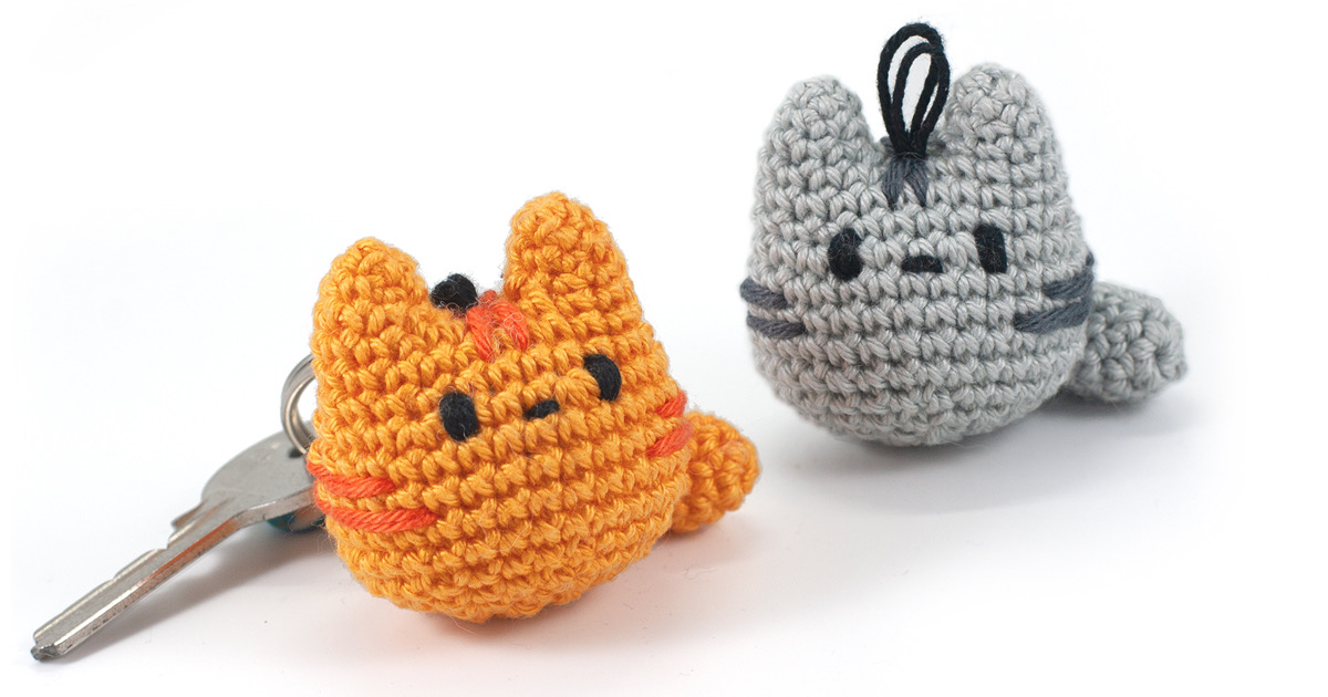 Two small crochet amigurumi cats in orange and grey beside a key