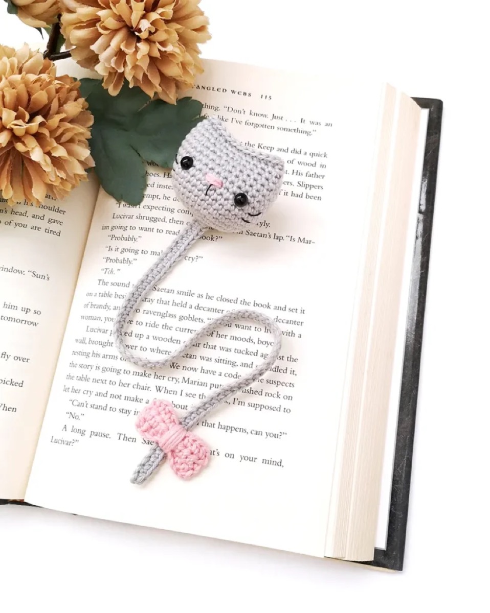 Grey crochet cat bookmark with a pink bow lying on an open book