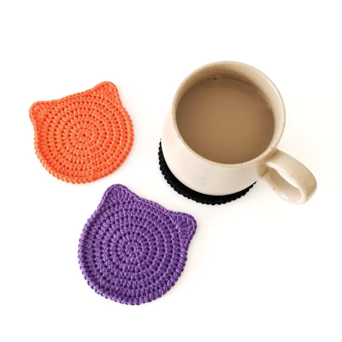 Orange and purple crochet cat face coasters beside a mug of coffee